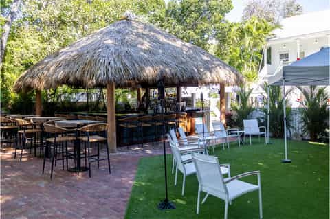 Tiki bar with thatched roof, high-top seating, lawn chairs, and green space at tropical resort property