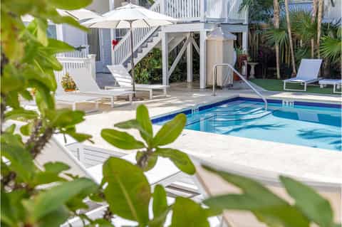 Resort pool area with white loungers, umbrellas, deck chairs, and elevated deck structure