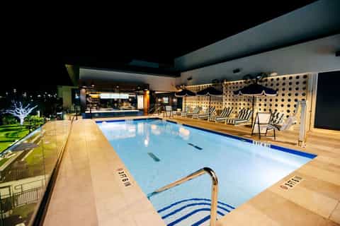 Indoor lap pool at night with modern lighting, wooden deck, and lounge chairs