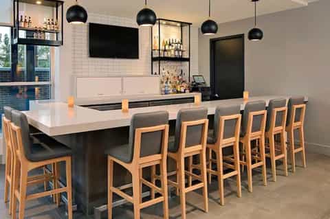 Modern bar counter with light wood stools, black pendant lights, and stocked shelving behind