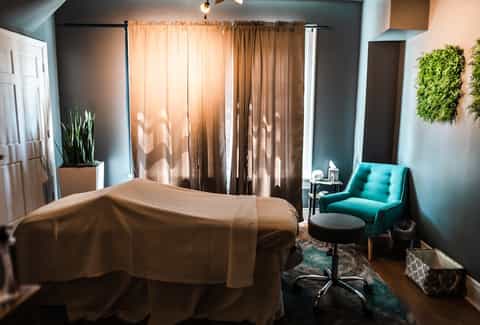 Compact hotel room with turquoise accent chair, draped windows, and modern minimalist decor