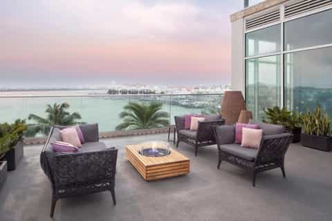 Waterfront terrace with black wicker chairs, pink cushions, fire pit, and bay views at dusk