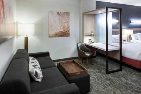 Hotel suite with living area, modern desk, open bathroom with red accents and glass partition