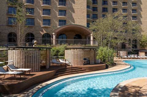 Resort pool area with geometric shade structures, lounge chairs, and brick residential buildings