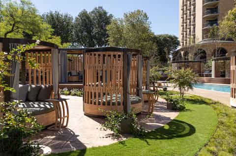 Wooden cabanas and seating areas with lounge chairs near resort pool and building