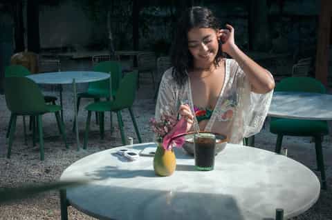 Woman dining outdoors at round table with flower arrangement and beverage
