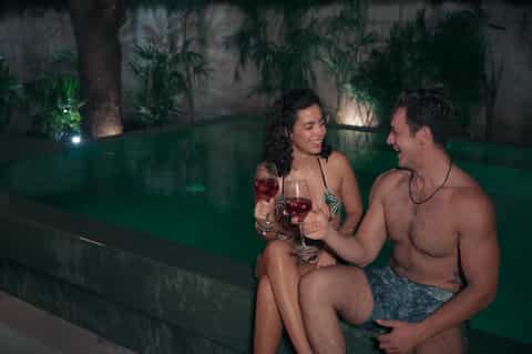 Couple enjoying wine in an illuminated indoor hot spring with tropical plants in background
