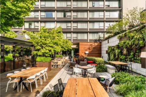 Outdoor courtyard with wooden dining tables, lush greenery, and covered lounge area