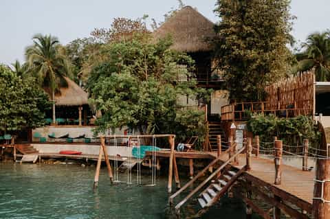 Tropical waterfront resort with thatched-roof buildings, wooden docks, and lush vegetation