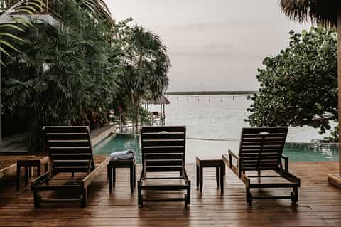 Waterfront lounge chairs on wooden deck overlooking bay with palm vegetation