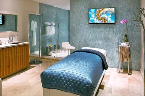 Spa treatment room with teal textured walls, massage bed, modern bathroom, and relaxation amenities