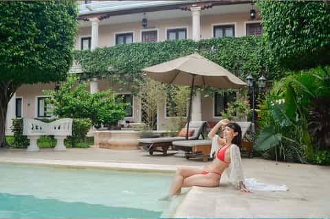 Woman in red swimsuit relaxing by small pool with ivy-covered colonial building