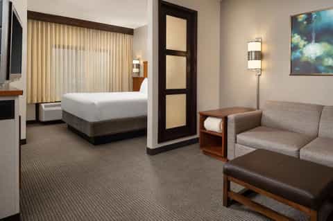 Hotel guest room with queen bed, sofa seating area, and modern neutral décor