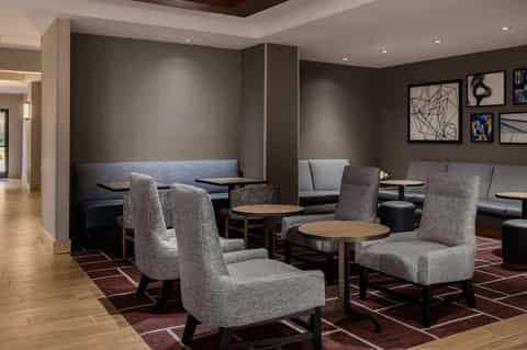 Contemporary hotel lounge with gray upholstered chairs, wooden tables, and neutral wall decor