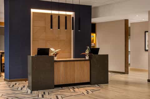 Hotel front desk with wooden slat design, dark marble panels, and modern lighting