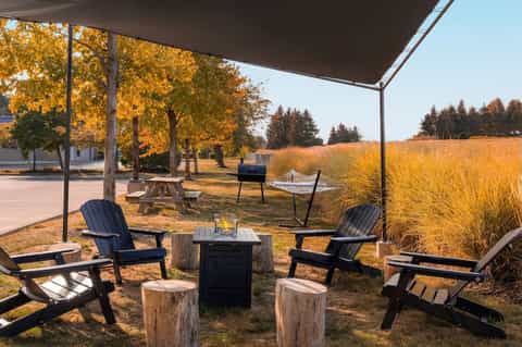 Outdoor fire pit area with Adirondack chairs, shade sail, and autumn landscape