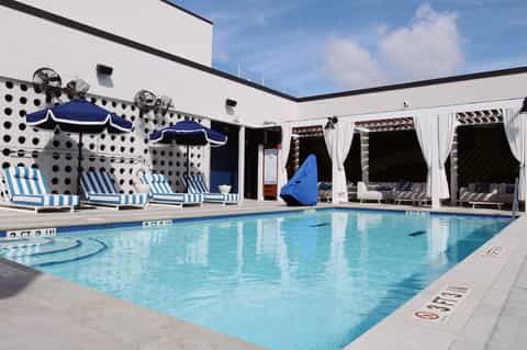 Indoor swimming pool with blue umbrellas, lounge chairs, and white cabanas
