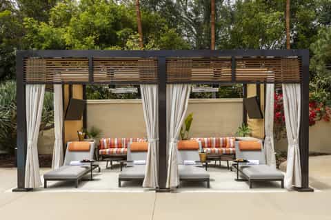 Outdoor cabanas with striped cushions, white curtains, lounge chairs, and desert landscaping