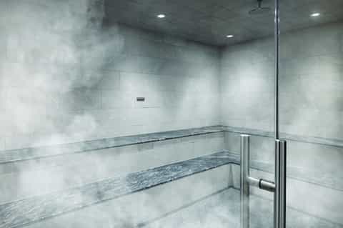 Modern steam room or sauna with marble tile benches and glass enclosure