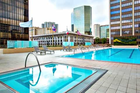 Outdoor rooftop pool with lounge chairs overlooking downtown city skyline and historic building