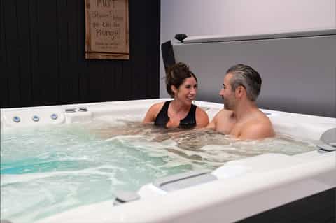 Couple relaxing in indoor hot tub with instructional sign on black wall behind them