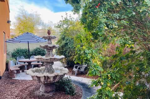Courtyard patio with stone fountain, striped umbrella, dining area, and ivy-covered walls