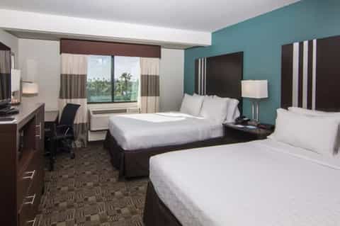 Hotel bedroom with two queen beds, teal accent wall, and ocean view windows