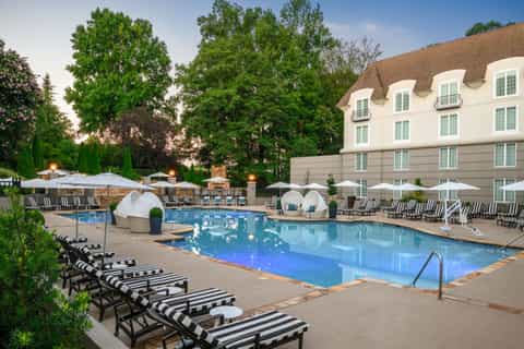 Resort pool area with striped lounge chairs, white umbrellas, and elegant colonial-style building