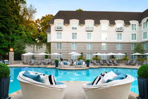 Elegant poolside lounge with white wicker chairs, umbrellas, and historic white hotel building