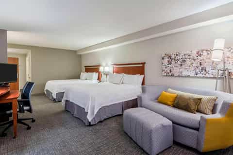 Hotel bedroom with two queen beds, sofa with yellow accent pillow, and work desk area