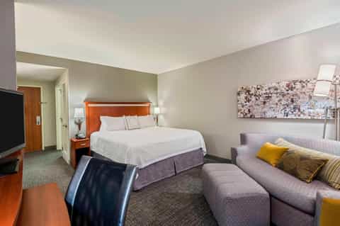 Hotel suite with queen bed, orange headboard, sofa with yellow pillows, and modern furnishings
