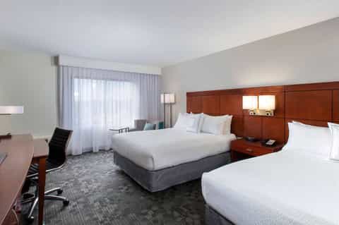 Hotel double queen bedroom with wood headboard, desk, and large windows with curtains
