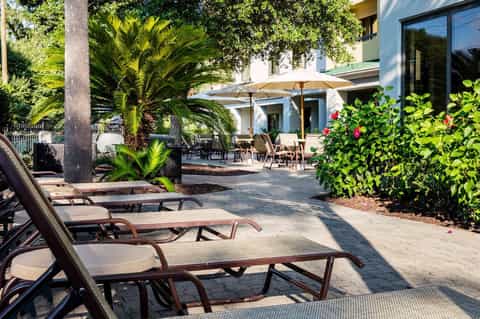 Resort patio with lounge chairs, beige umbrellas, lush green landscaping, and tropical plants