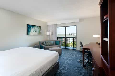 Hotel guest room with king bed, sitting area, and balcony overlooking grounds