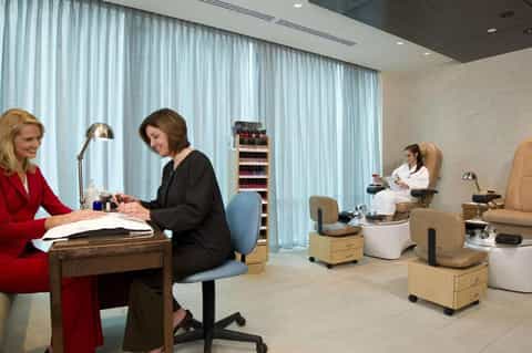 Spa reception area with nail stations, manicure chairs, and staff attending to guests