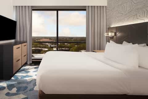Modern hotel bedroom with king bed, panoramic windows overlooking landscape, and contemporary furnishings