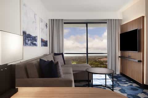 Luxury hotel suite living room with gray sofa, floor-to-ceiling windows overlooking landscape