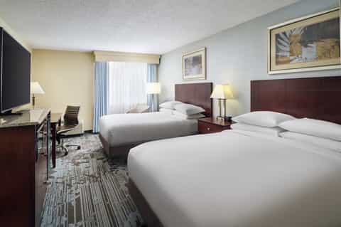 Hotel guest room with two queen beds, dark headboards, and desk area