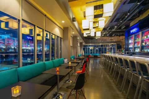 Contemporary hotel bar with turquoise seating, yellow geometric ceiling, and nighttime city views