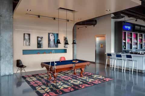 Game room with pool table, pendant lights, bar area with beverage cooler, and modern art