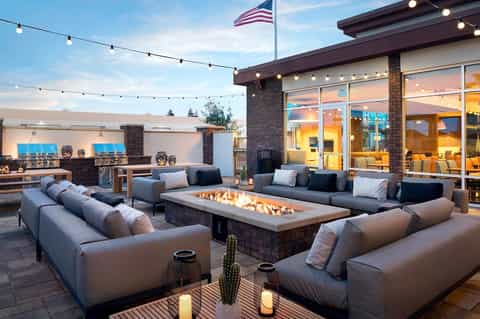 Luxury rooftop patio with fire pit, modern seating, string lights, and sunset views