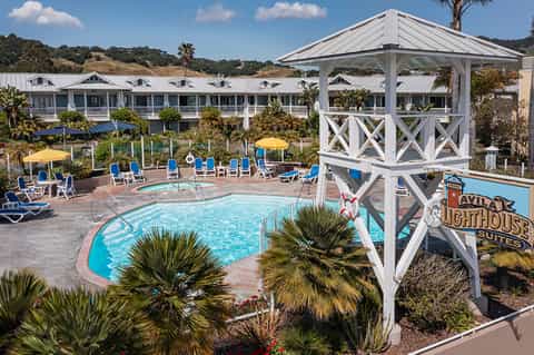 Resort pool area with blue loungers, yellow umbrellas, white gazebo, palm trees, and hillside accommodations