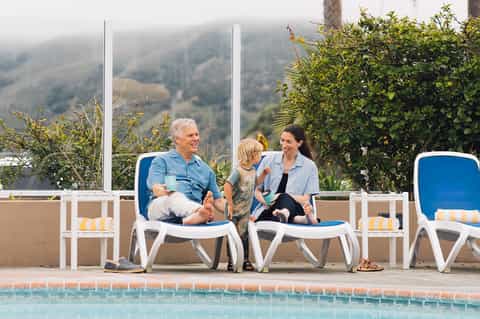 Family relaxing on blue lounge chairs by outdoor pool with mountain valley views