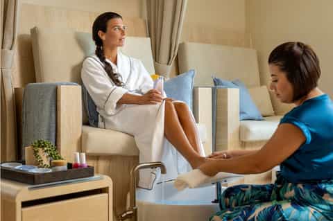 Spa treatment scene with woman in white robe receiving foot care from therapist in neutral salon