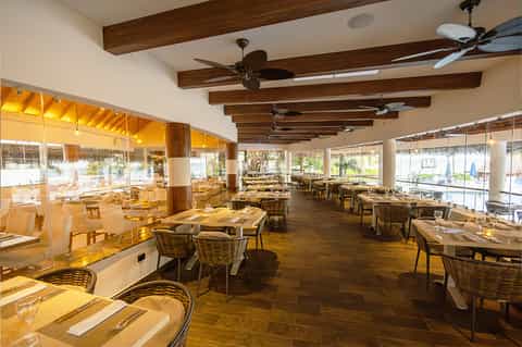 Modern resort restaurant with wooden beams, ceiling fans, and expansive waterfront windows