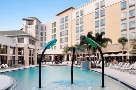 Contemporary hotel pool with teal water, palm trees, and lounge chairs with umbrellas