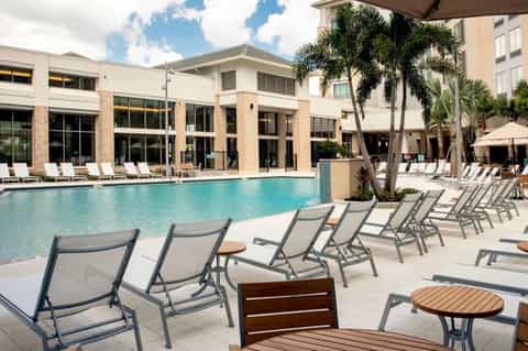 Resort pool deck with lounge chairs, palm trees, and contemporary building architecture
