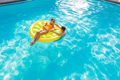 Two children playing on a yellow inflatable float in a bright turquoise swimming pool