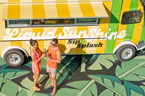 Couple holding drinks at a colorful yellow and green food truck labeled 'Liquid Sunshine'