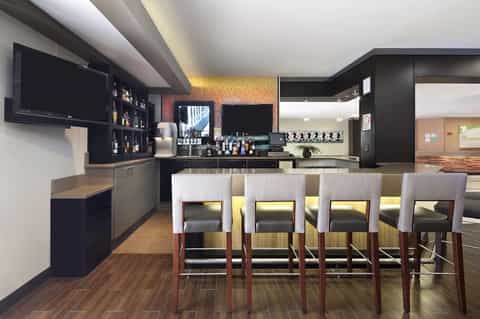 Hotel bar lounge with black cabinetry, bar seating, and amber accent lighting